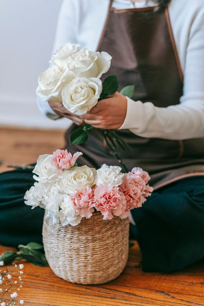 Crop unrecognizable woman florist in apron arranging bouquet with white roses and colorful chrysanthemums in light room